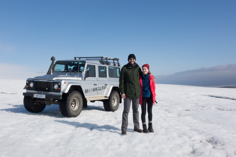 A couple standing on a glacier near a 4x4